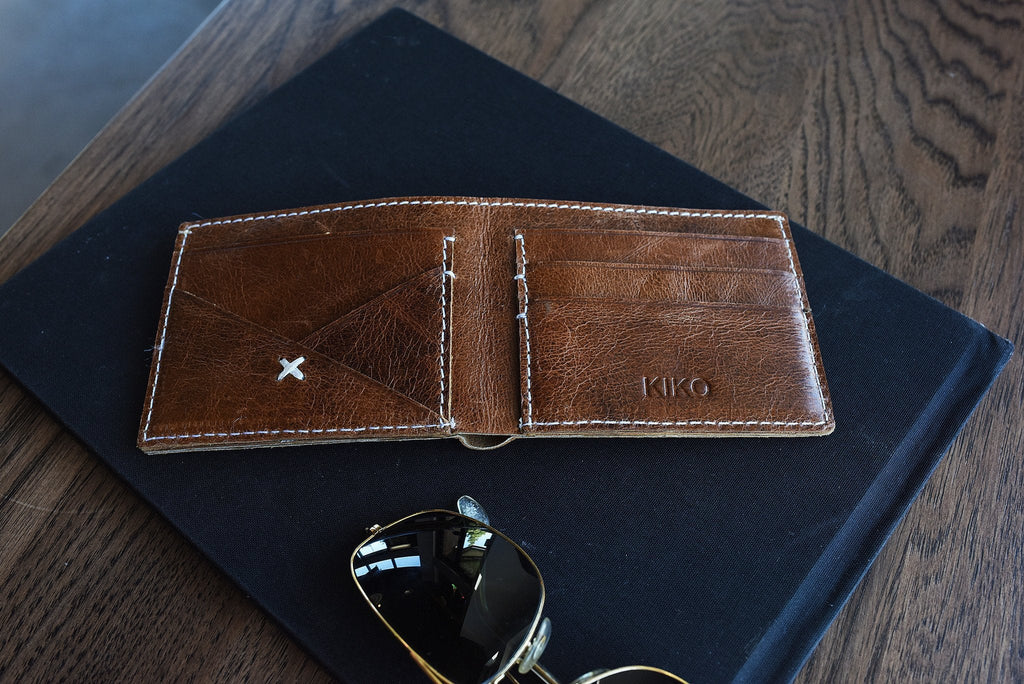 Minimalist Leather X bifold wallet with white stitches and card slots on natural leather background