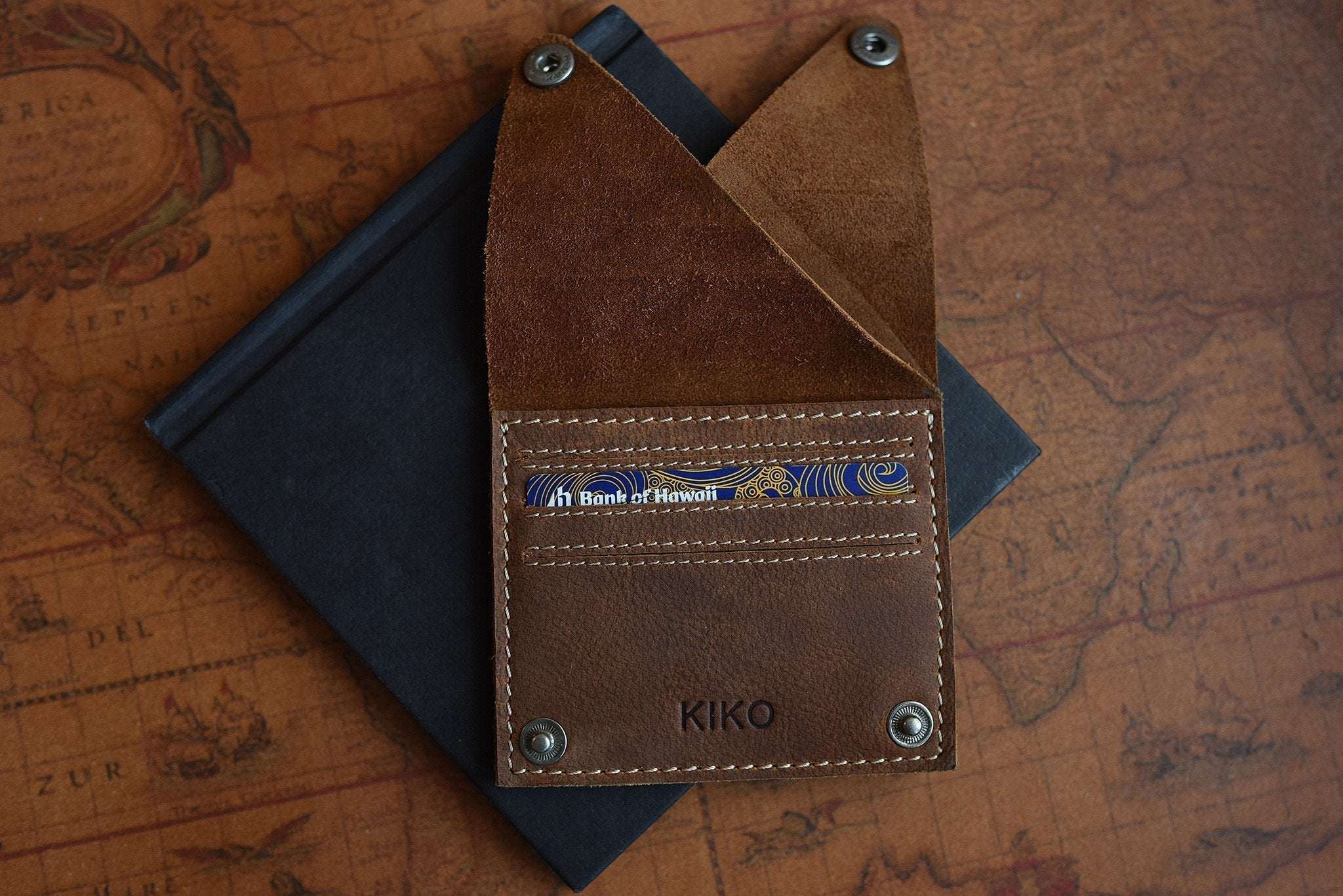 Kiko Wing fold wallet in soft leather with geometric pattern, white stitching, and secure buttons, compact design for cards and cash